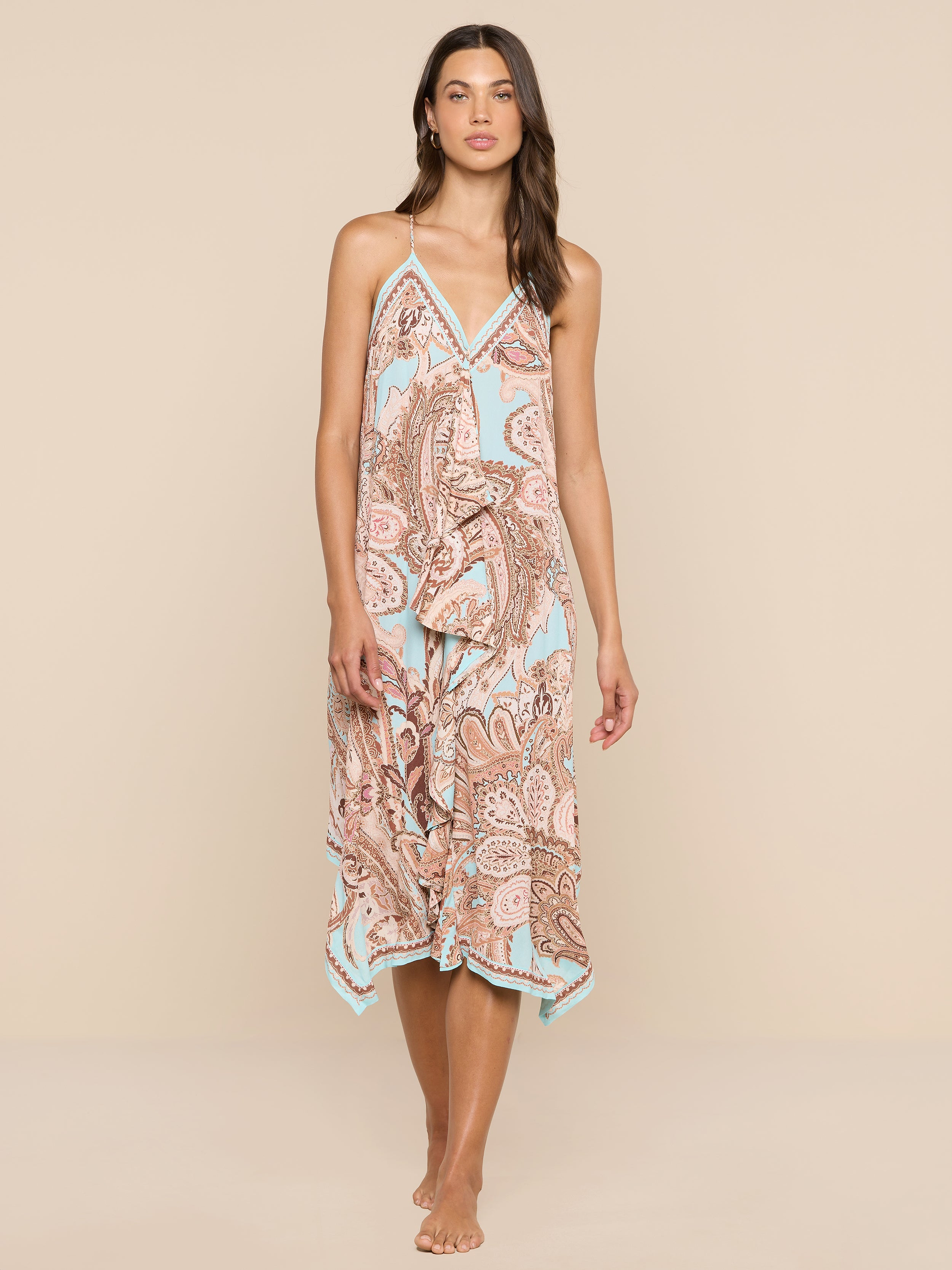 A woman stands barefoot against a white background, wearing the Elise Cover-Up Dress, which features a paisley print, halter neckline, V-neckline, and a flowy midi silhouette.