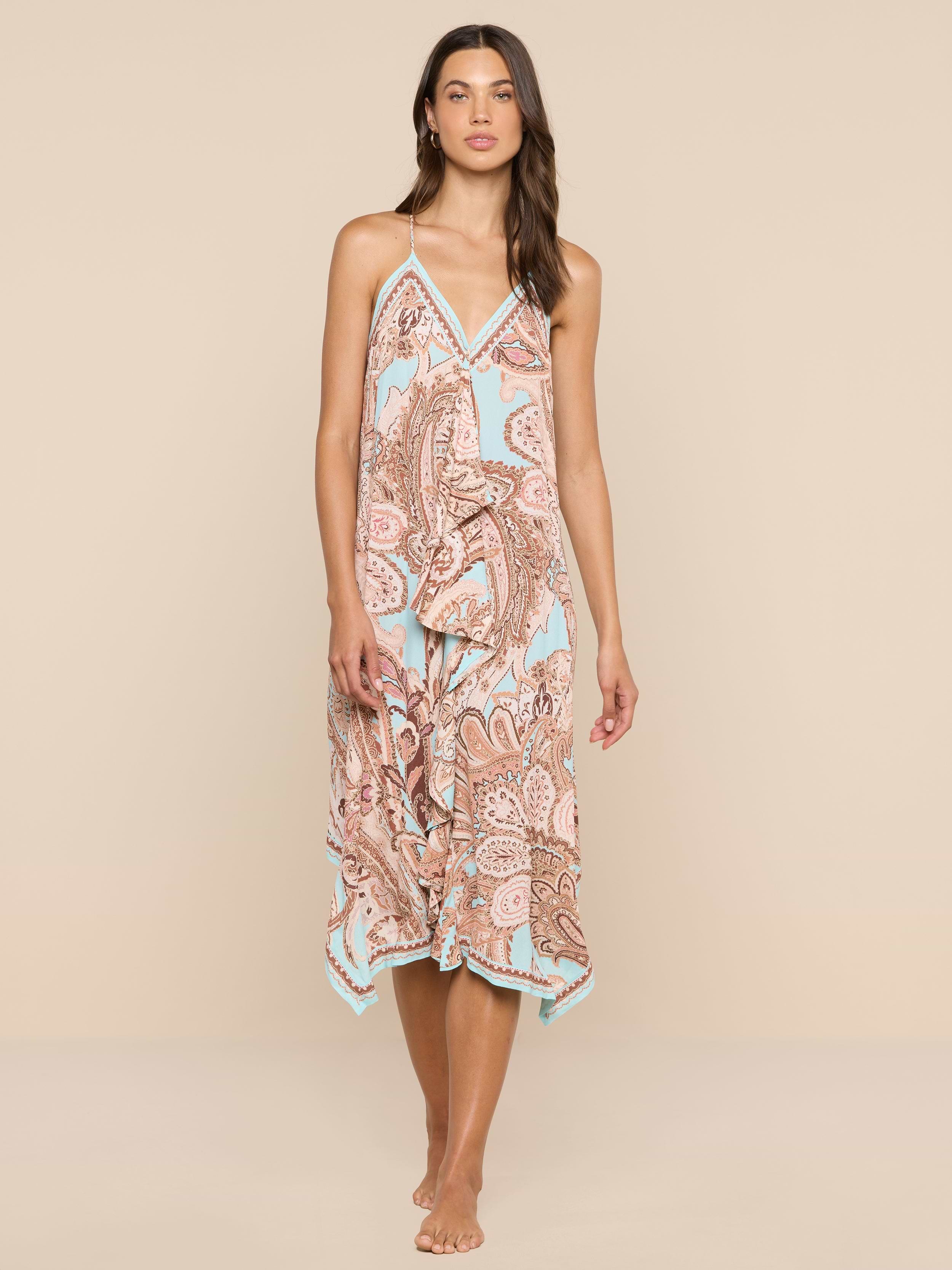 A woman stands barefoot against a white background, wearing the Elise Cover-Up Dress, which features a paisley print, halter neckline, V-neckline, and a flowy midi silhouette.