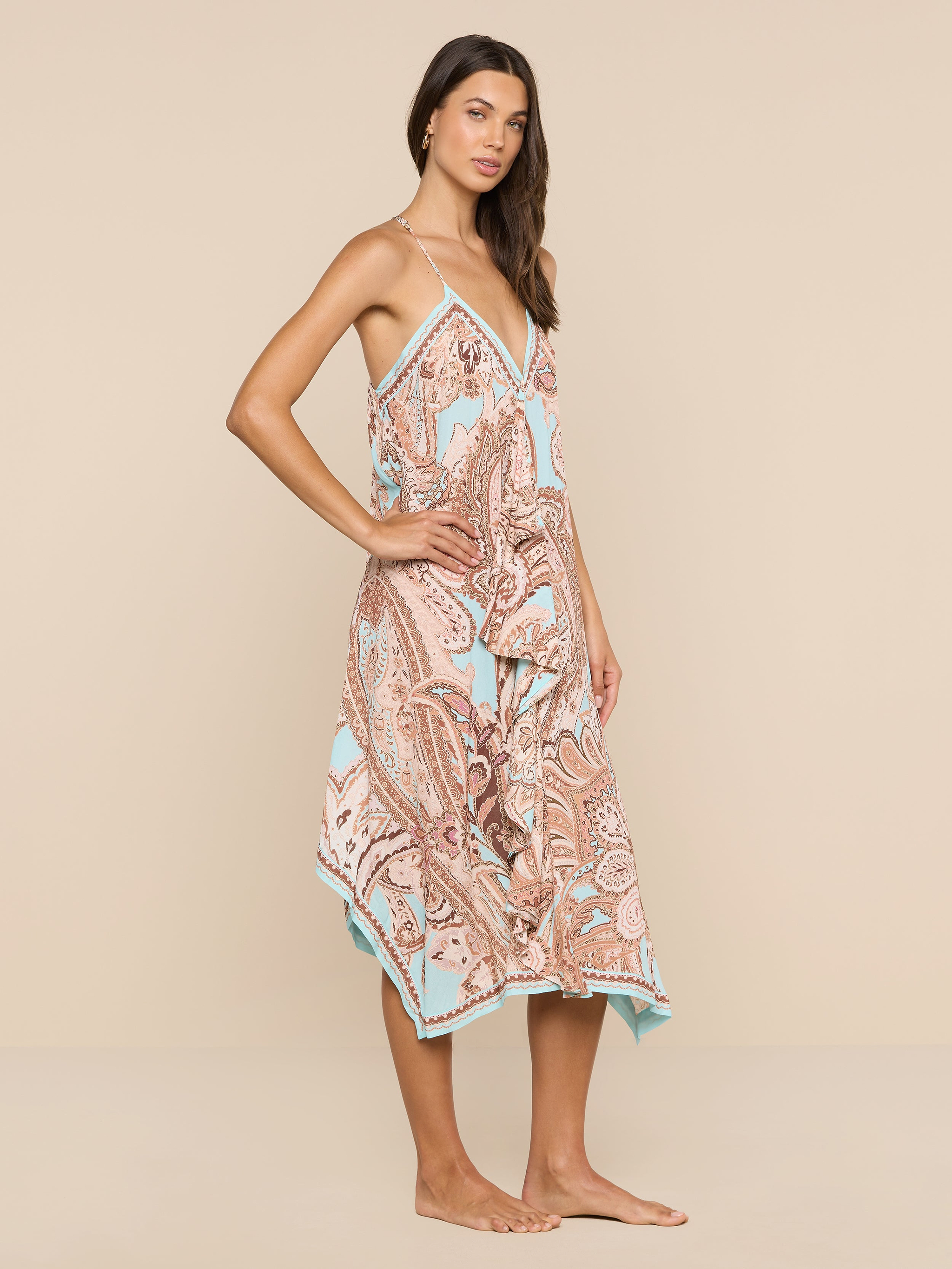 A woman stands barefoot against a plain white background, wearing the Elise Cover-Up Dress—a sleeveless, flowy halter midi dress featuring a paisley print in soft pastel colors.