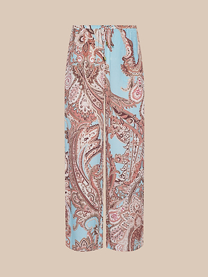 The Geraldine Cover-Up Pant features a blue and brown paisley print, wide-leg design, elastic waistband, and drawstring for a relaxed fit, shown against a beige background.