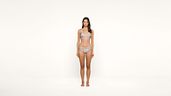 A woman stands barefoot against a plain white background, wearing a matching silver and gray bikini. She faces forward with a neutral expression and relaxed posture.