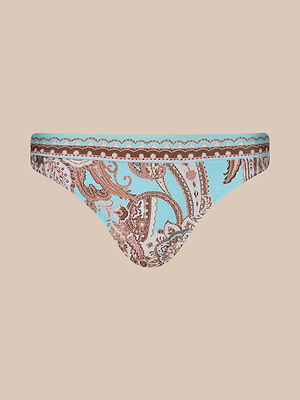 The Nicole Bikini Bottom features an intricate paisley print on a light blue background with scalloped trim at the waistband. Made from stretch nylon, its shown against a plain beige backdrop.