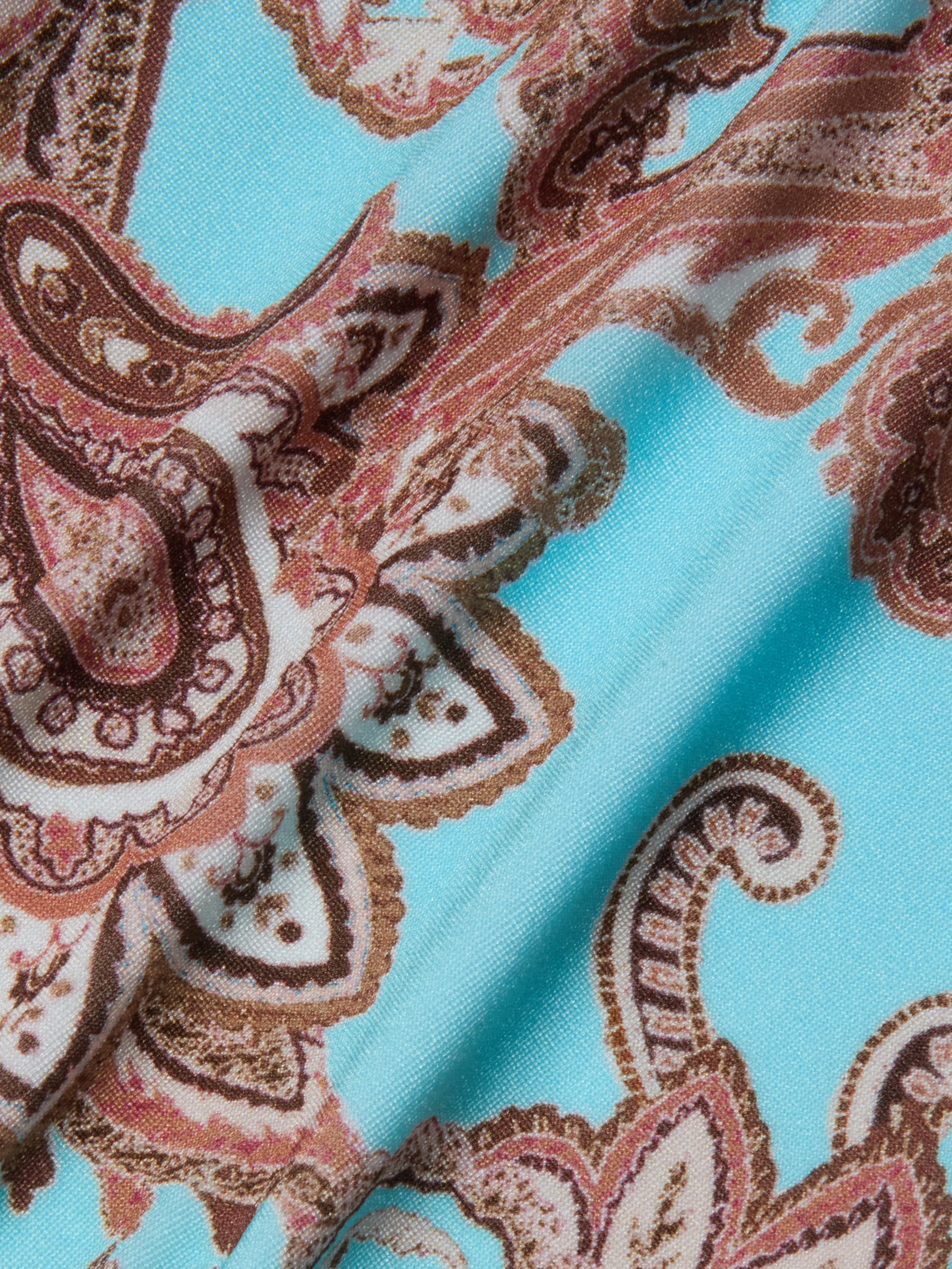 A close-up of the Violet String Bikini Bottom showcases light blue fabric adorned with a paisley pattern in brown, cream, and white. The swirling shapes and intricate details are reminiscent of a classic string bikini bottom, with the fabric appearing slightly folded.