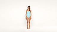 A woman stands facing forward against a plain white background, wearing a light blue one-piece swimsuit.