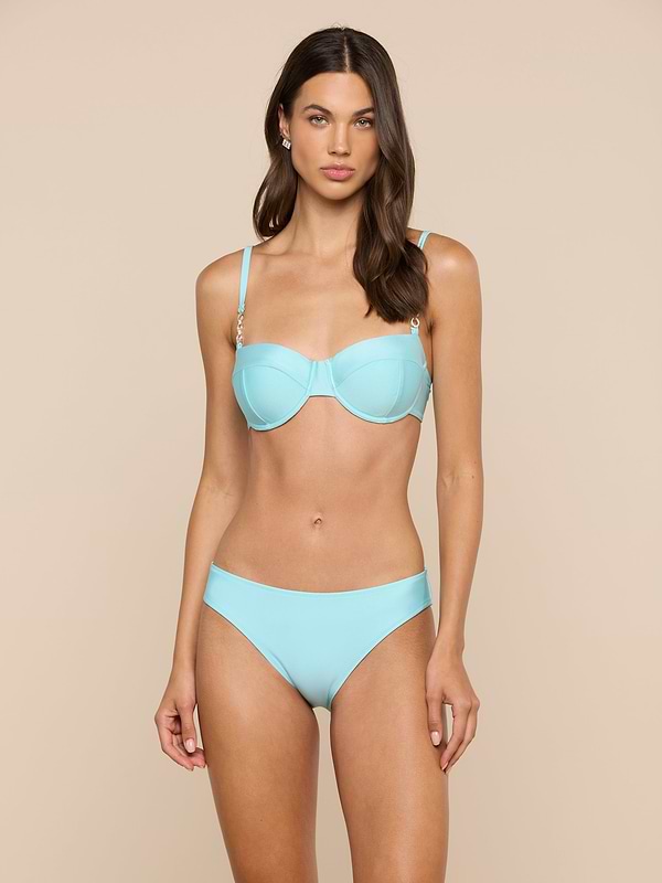 A woman stands against a plain light background, wearing the Alexandria Bikini Top in ice blue with a neutral expression.