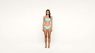 A woman stands barefoot against a plain white background, wearing a light blue bikini.