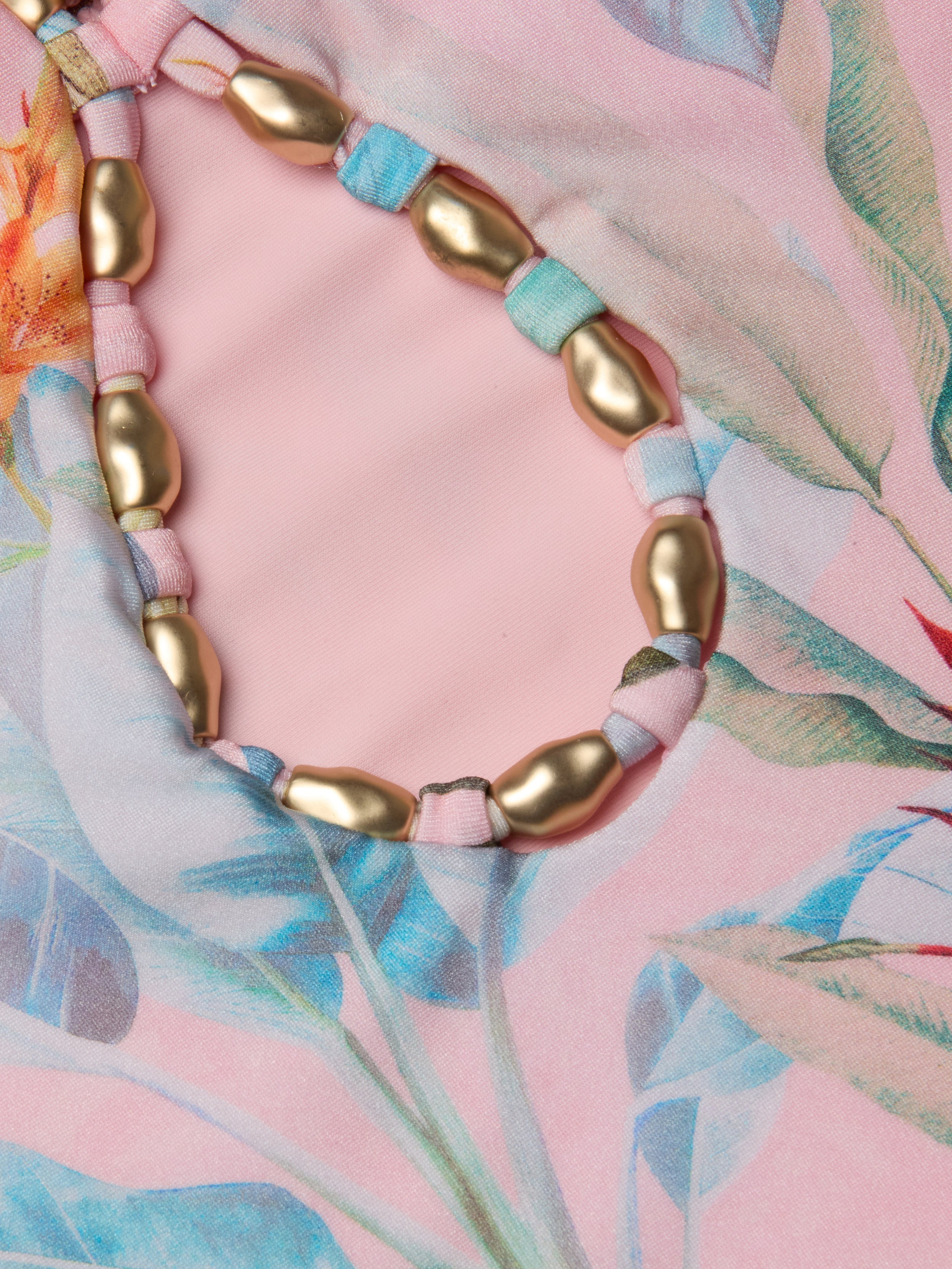 Close-up of the Opus Halter One-Piece Swimsuit in pink floral fabric, featuring a loop of gold oval beads threaded on multicolored fabric strips.