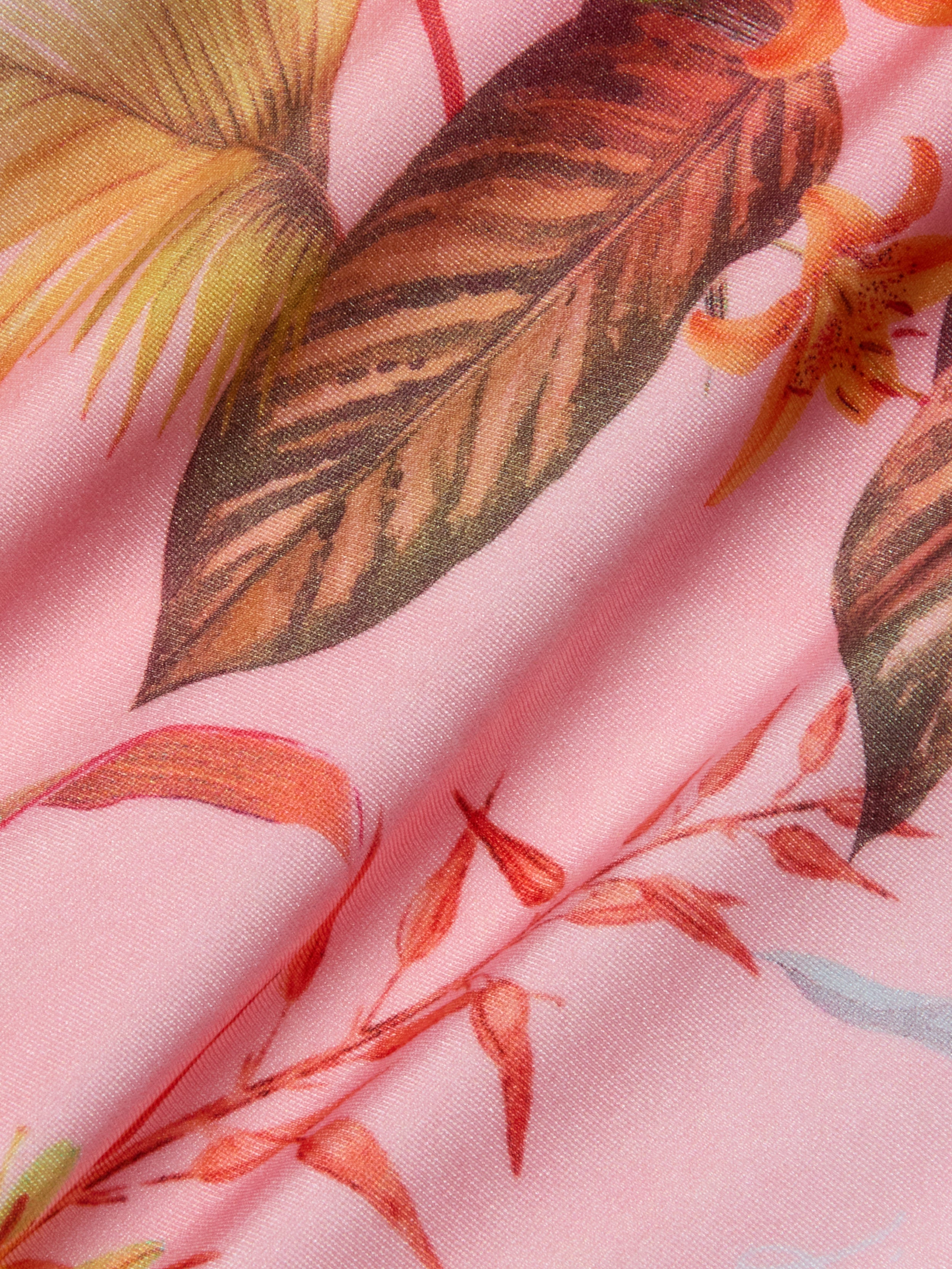The Remi One-Piece Swimsuit features pink fabric adorned with a detailed tropical floral and palm leaf print in brown, orange, and yellow hues. The softly crinkled material enhances the texture and vibrant botanical pattern—ideal for crafting an eye-catching one-piece or high-leg swimsuit.