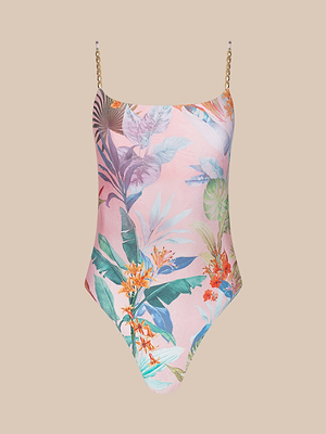 The Remi One-Piece Swimsuit features a high-leg cut and thin chain straps, with a tropical floral and palm leaf print in pink, green, blue, and orange on a light pink background.