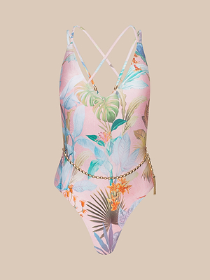 The Breana Plunge One-Piece Swimsuit features a palm print with pink tropical florals, blue and green leaves, orange flowers, crisscross back straps, and a gold chain belt, shown on a beige background.