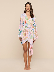 A woman stands facing forward, wearing the Kohima Cover-Up Dress—a pastel floral wrap dress with bell sleeves and a tie at the waist—against a plain white background.