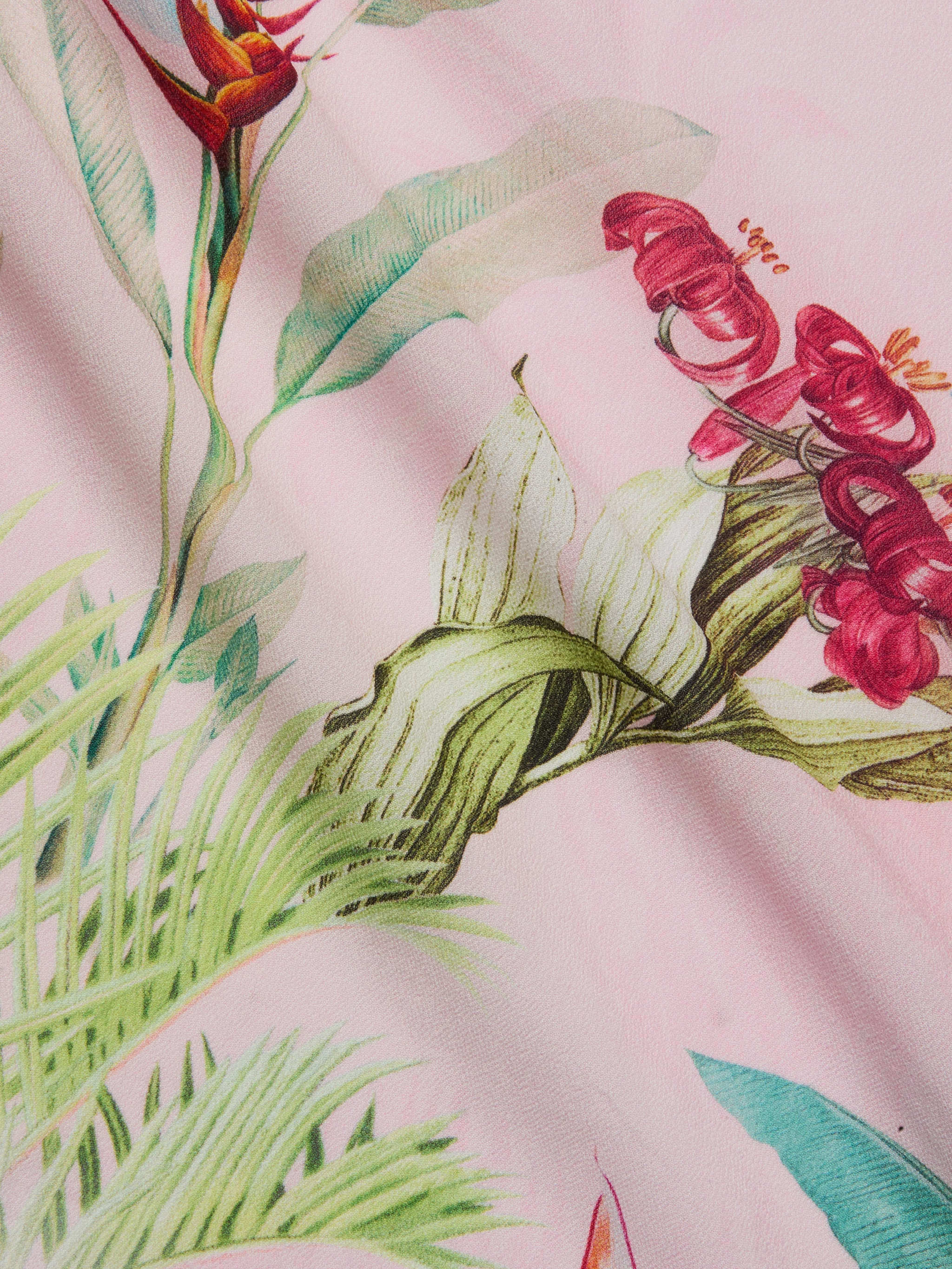 A close-up of the Kohima Cover-Up Dress, showcasing its pink fabric adorned with a colorful botanical print of red flowers, green leaves, and delicate stems—perfect for resort-style poolside wear.