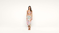 Woman standing barefoot against a plain white background, wearing a pastel floral bikini top and matching wrap skirt, with arms relaxed by her sides.