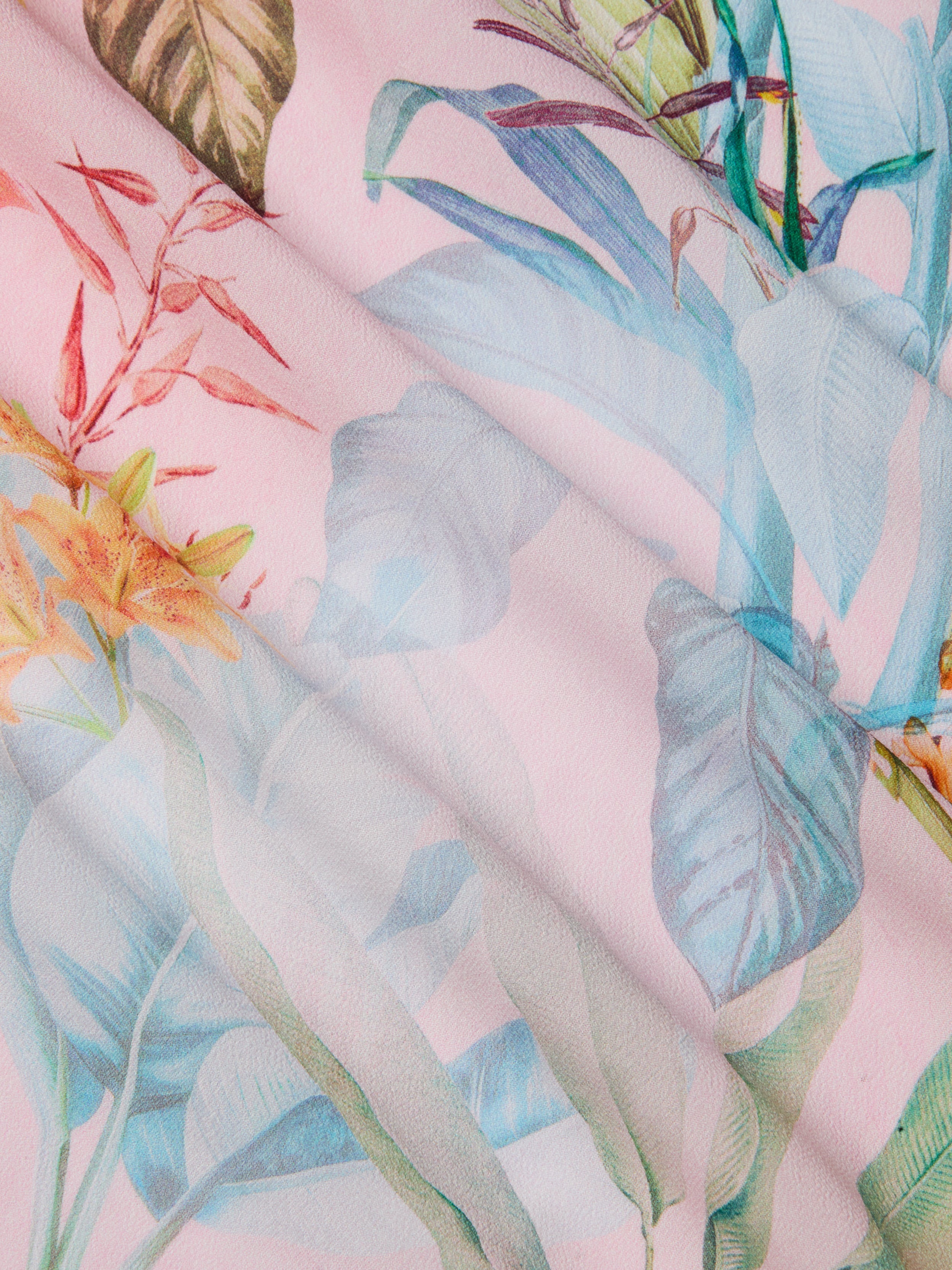 The Marena Sarong features a pastel floral fabric with a pink background and delicate blue, green, and orange leaves in a soft, watercolor pattern—perfect as a vacation sarong or beach cover-up.