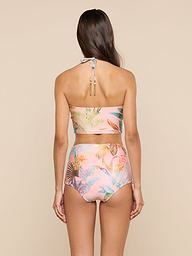 A woman with long brown hair is seen from the back, wearing the Siwan Midkini—a pastel floral two-piece swimsuit with a longline bikini top and high-waisted bottoms—standing against a plain light background.
