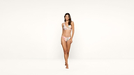 A woman wearing a pastel floral bikini stands barefoot against a plain white background, looking forward with a neutral expression.
