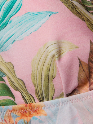 Close-up of the Lexie Bikini Top, featuring gathered fabric with a palm leaf and tropical flower print in green, yellow, blue, and orange on a pink background. The bottom edge is stitched with white thread.
