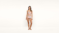 Woman standing barefoot against a plain white background, wearing a matching two-piece swimsuit with a pastel floral print. She looks ahead with a neutral expression and relaxed posture.