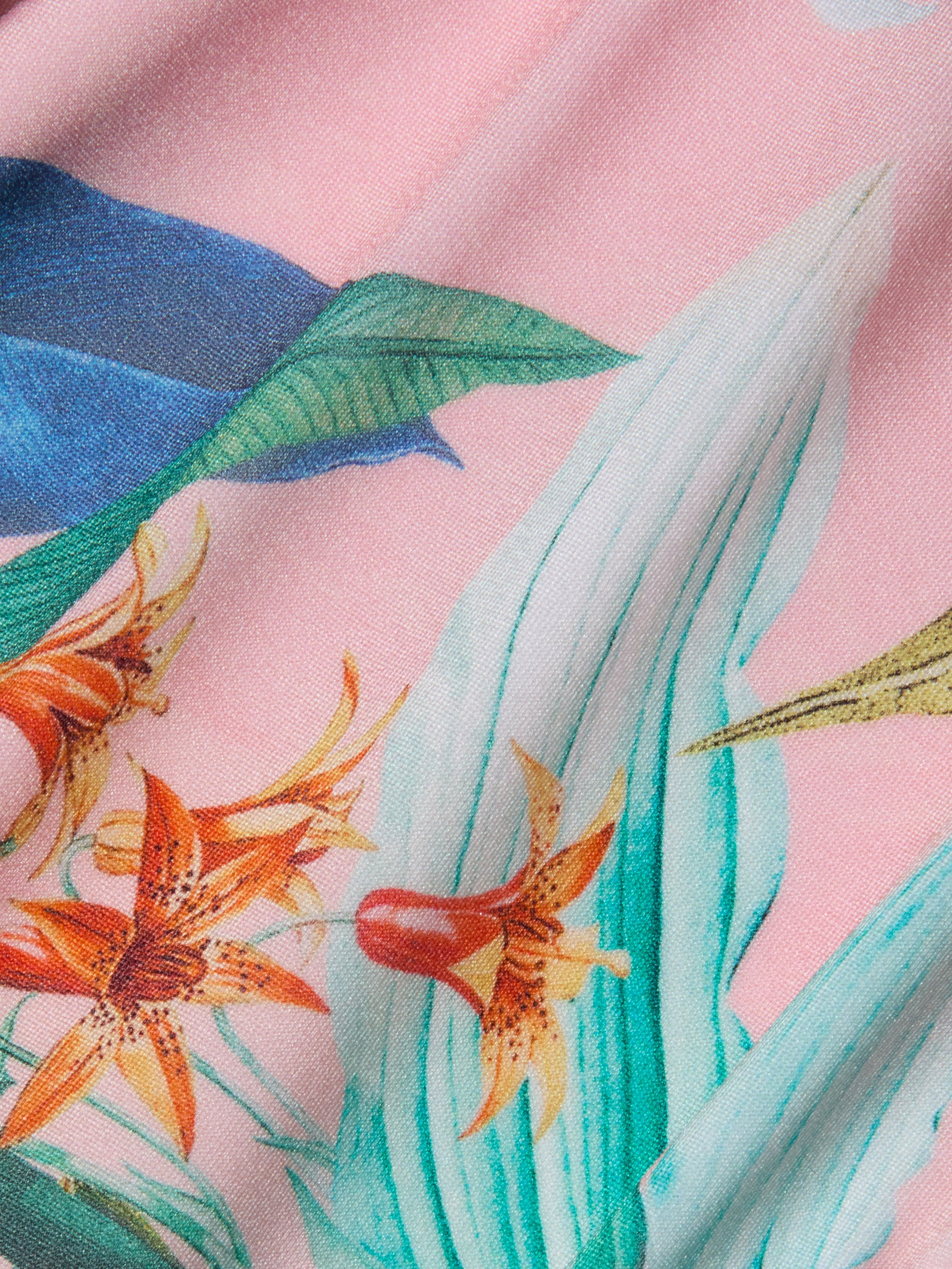 Close-up of colorful tropical floral fabric featuring orange flowers, green and blue leaves, and a pink background—ideal for the Linda Swim Skort, which offers UPF 50 sun protection.