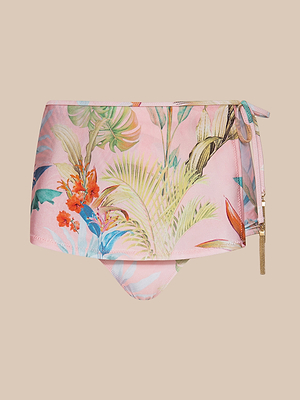 The Linda Swim Skort features a pink base with a vibrant tropical floral print in green, red, and blue, UPF 50 sun protection, and a gold zipper with a tassel detail on the right side.