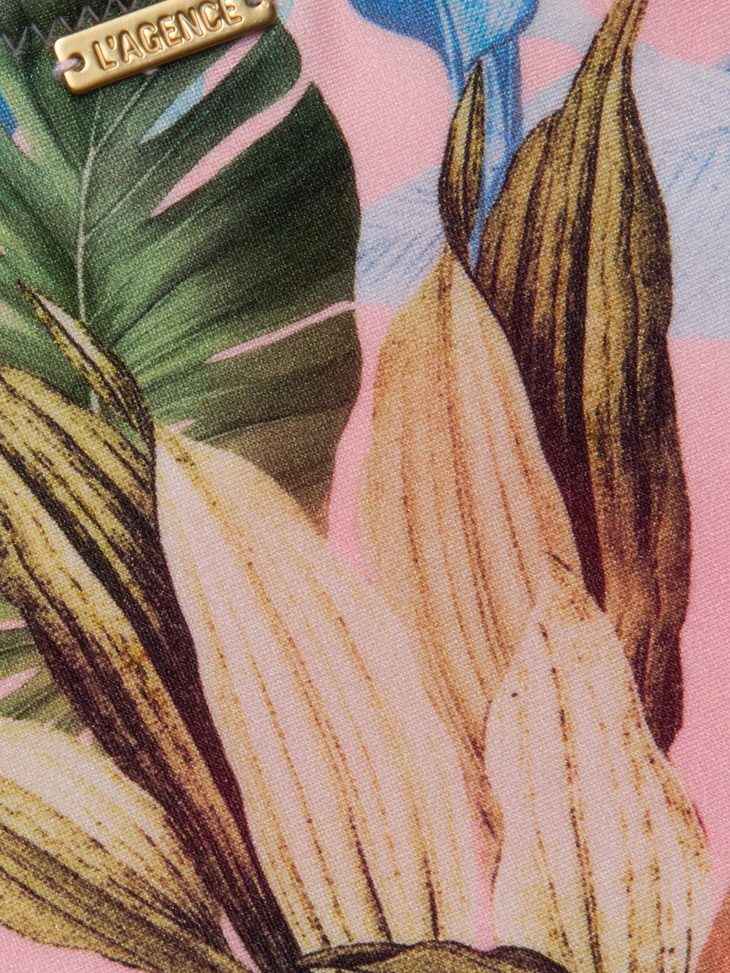 Close-up of the Nicole Bikini Bottom, showcasing a tropical palm leaf print in green, yellow, and brown on a pink background, with a small metal LAGENCE label.