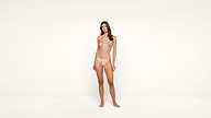 A woman stands barefoot against a plain white background, wearing a pastel-colored bikini with a floral pattern.
