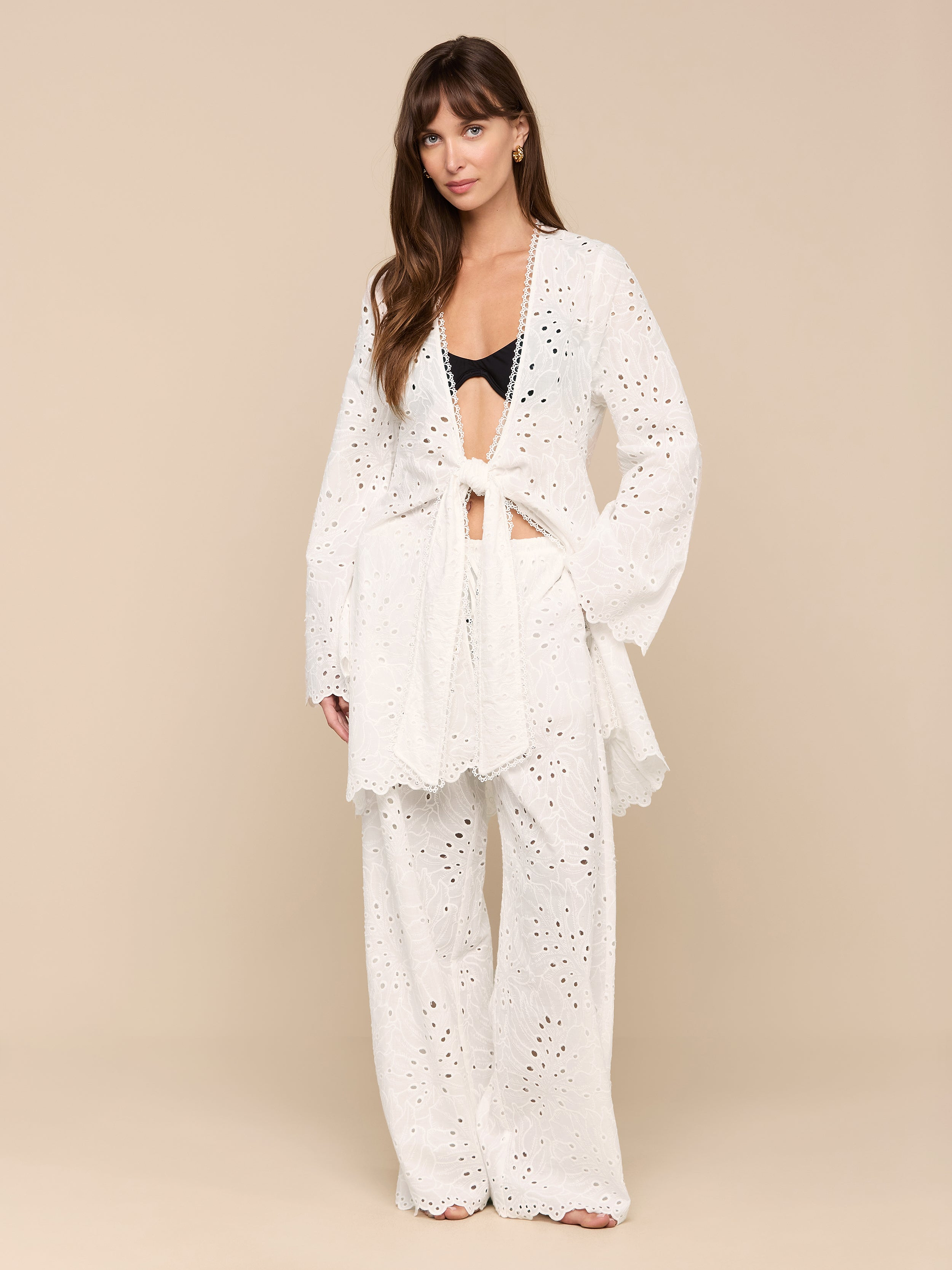 A woman stands against a plain white background wearing the Navaeh Cover-Up Kimono layered over a black bralette and matching wide-leg pants. Her hair is down, and she looks calmly at the camera.