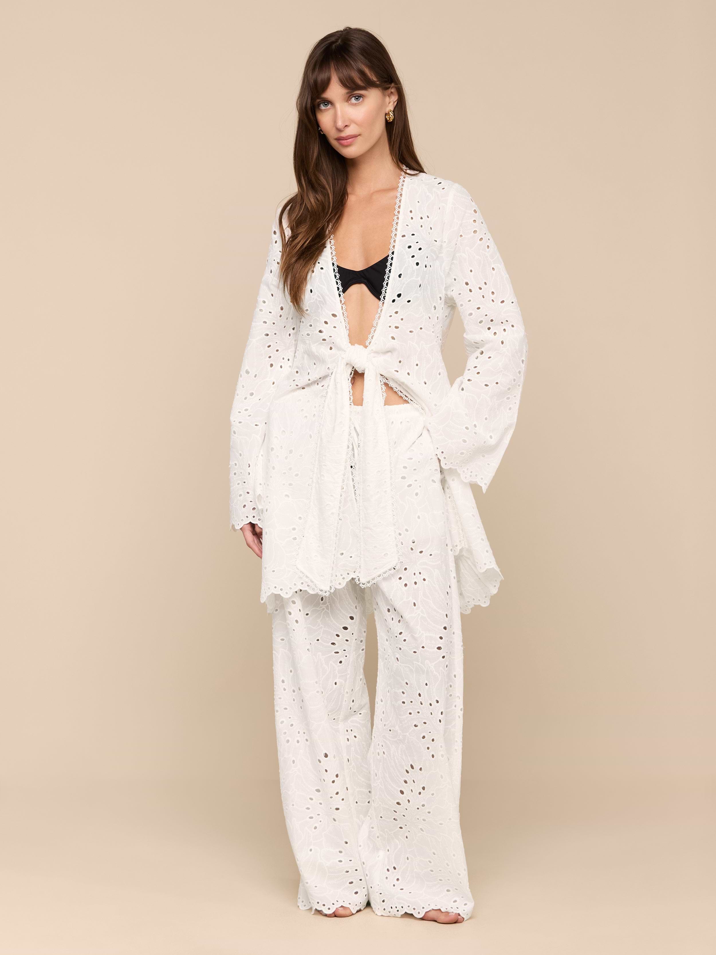 A woman stands against a plain white background wearing the Navaeh Cover-Up Kimono layered over a black bralette and matching wide-leg pants. Her hair is down, and she looks calmly at the camera.