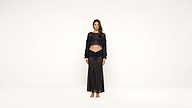 A woman stands barefoot against a white background, wearing a sheer black long-sleeve crop top and a matching sheer black maxi skirt.