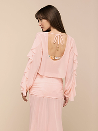 Woman in the Ambala Cover-Up Top—a light pink, sheer mesh top with ruffled sleeves and an open back—looking to her left. The cropped silhouette stands out against the plain, light-colored background.