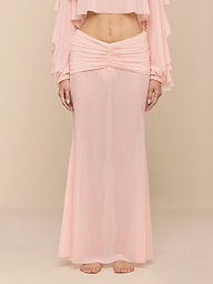 A person stands barefoot on a white background, wearing the light pink Mahe Mesh Cover-Up Skirt styled as a mermaid skirt and a matching long-sleeve top that reveals their midriff. The person’s head is not visible.