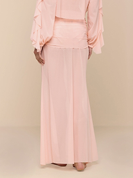 A person wearing a light pink, long-sleeved blouse and a matching pink Mahe Mesh Cover-Up Skirt stands barefoot against a plain white background, with their hands resting at their sides.
