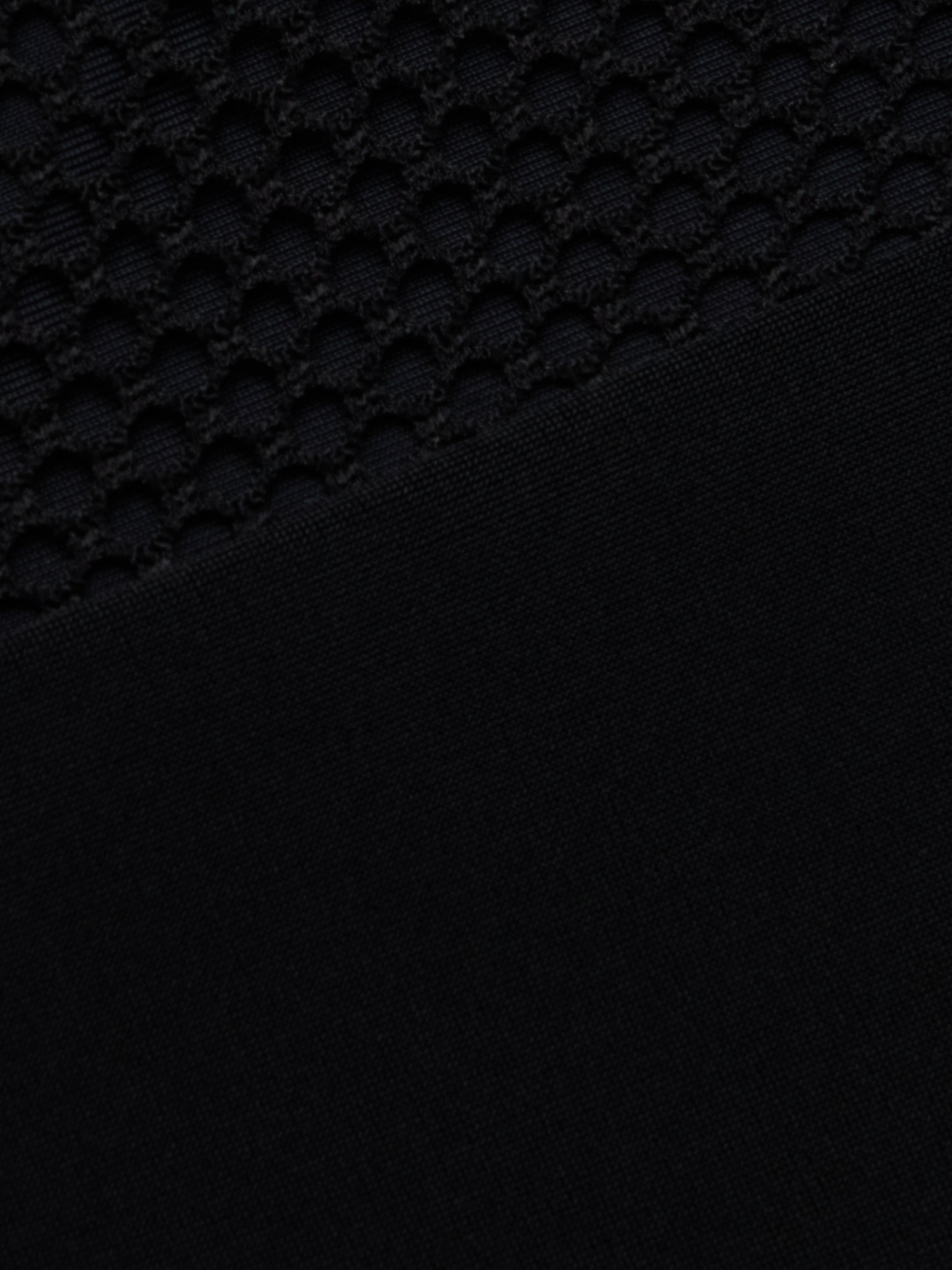 Close-up of the Anastasia Swim Top—a black polo-style top with a textured, honeycomb pattern on the upper half and a sleek, solid black finish on the lower half—perfect for showcasing beachside sophistication.