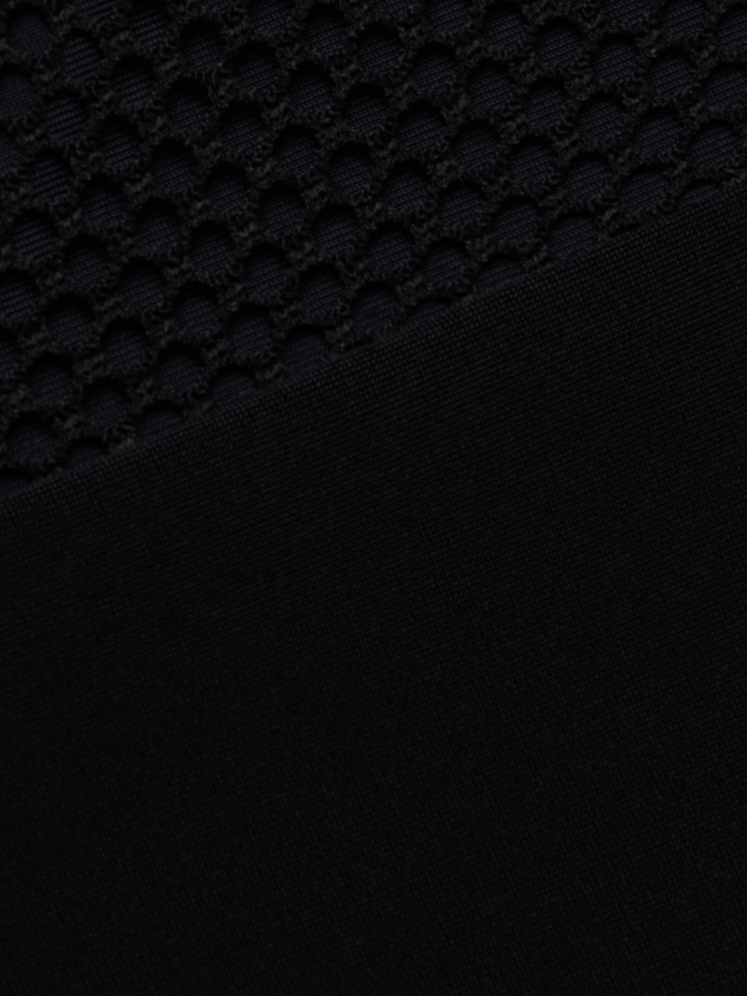 Close-up of the Anastasia Swim Top—a black polo-style top with a textured, honeycomb pattern on the upper half and a sleek, solid black finish on the lower half—perfect for showcasing beachside sophistication.