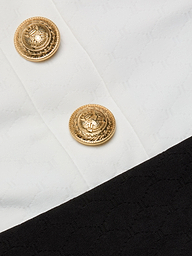 Close-up of two gold decorative buttons with an eagle emblem on the Mila One-Piece Swimsuit, set against textured white fabric with a black border at the bottom right corner, evoking a touch of French glamour.