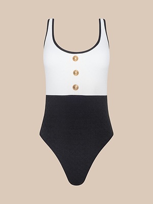 The Mila One-Piece Swimsuit features a white top, black bottom, and three gold buttons with black trim. Inspired by French glamour, this swimwear classic delivers elevated style on a beige background.