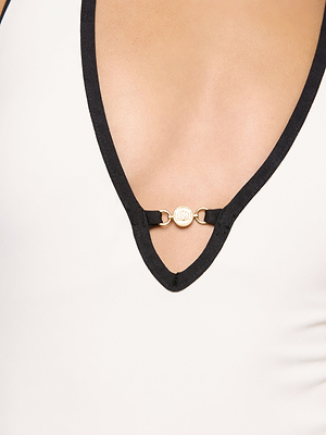 Close-up of the Breana Plunge One-Piece Swimsuit: white with black trim, gold clasp detail, and plunge neckline. Features UPF 50 protection and removable cups for comfort. Skin is visible above the neckline.