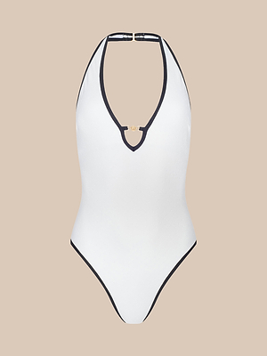 The Breana Plunge One-Piece Swimsuit features a white design with black trim, removable cups, and a gold accent at the front neckline, shown against a plain beige background.