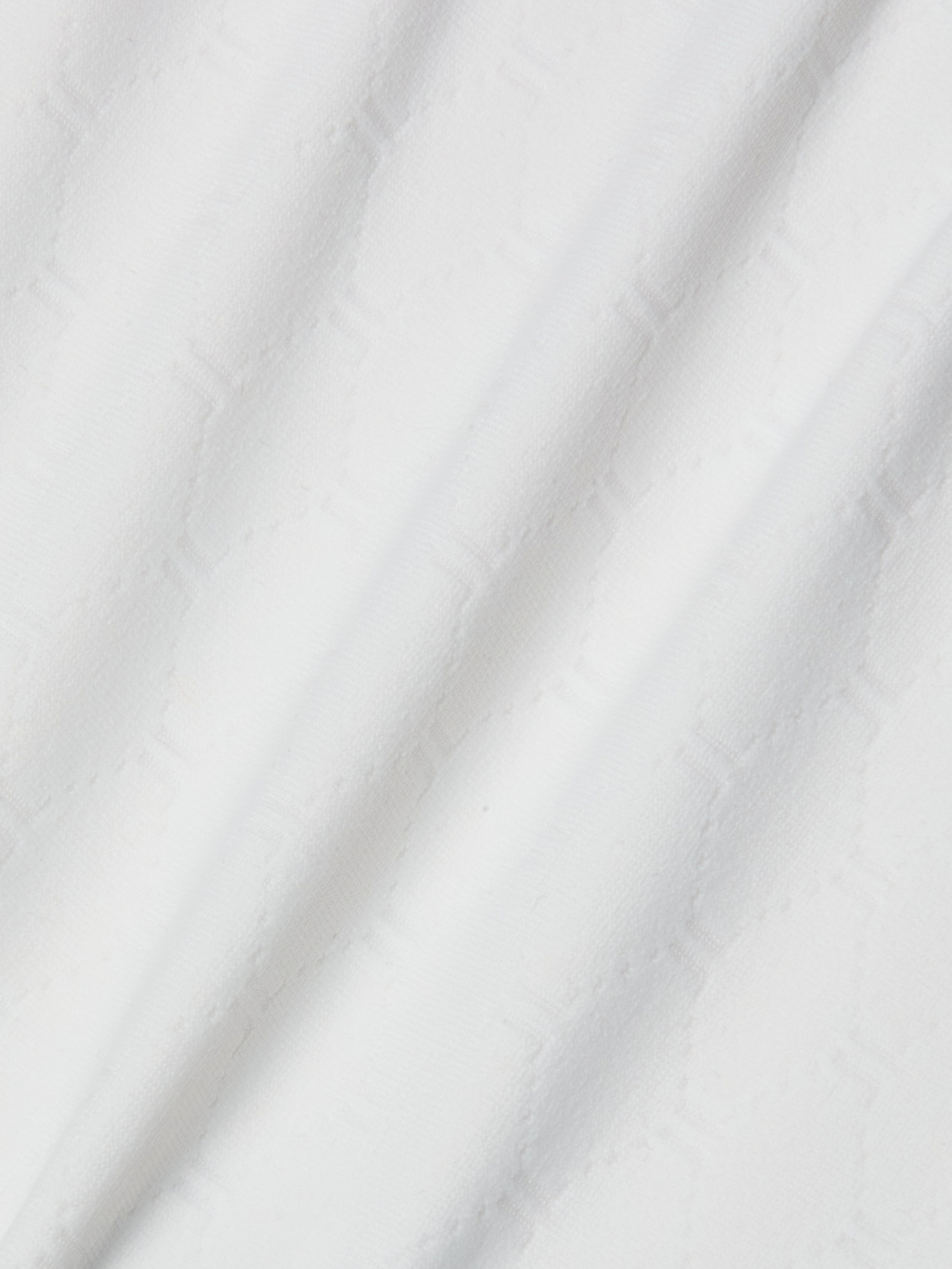 A close-up of white textured fabric with a subtle geometric hexagon pattern and soft diagonal folds, similar to the material used in the Violet String Bikini Bottom, which offers moderate coverage and UPF 50 protection.
