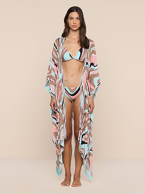 A woman stands barefoot against a beige background, wearing an abstract swirl print bikini and the Kara Kimono Cover-Up—a sheer, pastel beachwear piece with wide sleeves that drapes to the floor.