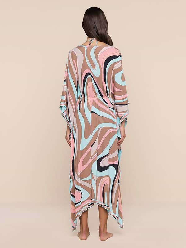 A woman stands barefoot facing away, wearing the Kara Kimono Cover-Up crafted from flowing viscose crepe with a pink, blue, beige, black, and white abstract swirl pattern. The plain white background highlights this stylish piece—perfect as a beachwear cover-up.