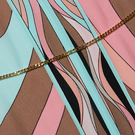 The Kara Kimono Cover-Up, crafted from viscose crepe fabric featuring an abstract pattern in pastel pink, blue, brown, and black shapes, is accented by a gold chain draped diagonally across it.