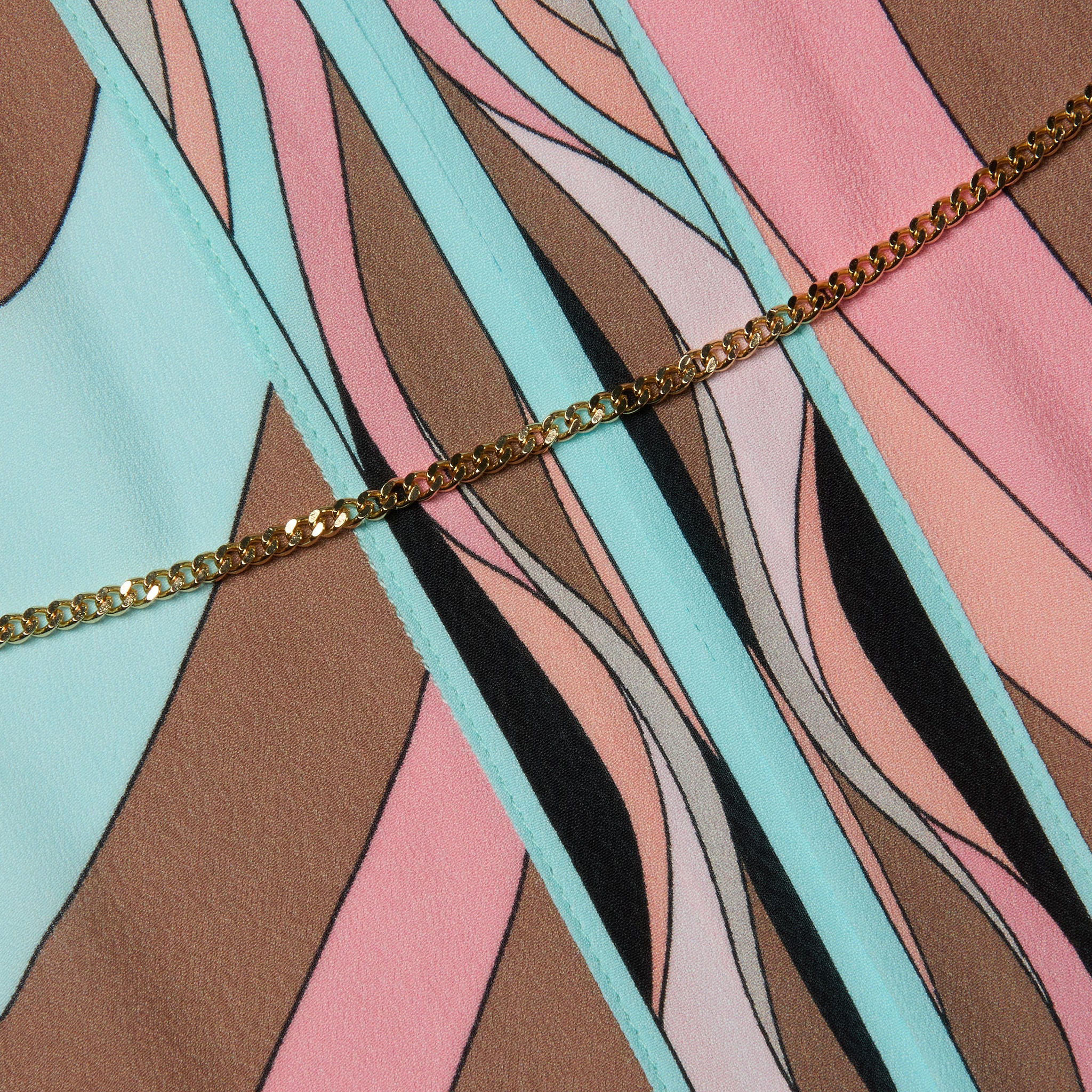 The Kara Kimono Cover-Up, crafted from viscose crepe fabric featuring an abstract pattern in pastel pink, blue, brown, and black shapes, is accented by a gold chain draped diagonally across it.