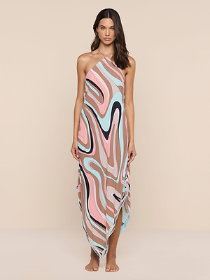A woman stands barefoot against a beige background wearing the Elise Cover-Up Dress—an abstract swirl print halter midi with a sleeveless design, flowing handkerchief hem, and asymmetric neck tie for an effortless, modern style.