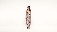 A woman stands barefoot against a white background, wearing a sleeveless dress with a pink, blue, and beige abstract swirl pattern.