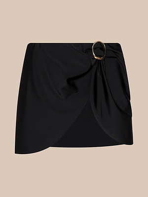 The Chandra Cover-Up Skirt is a black, high-waisted mini skirt featuring a draped front and bold gold buckle detail—ideal for chic, effortless poolside glam—shown on a neutral beige background.