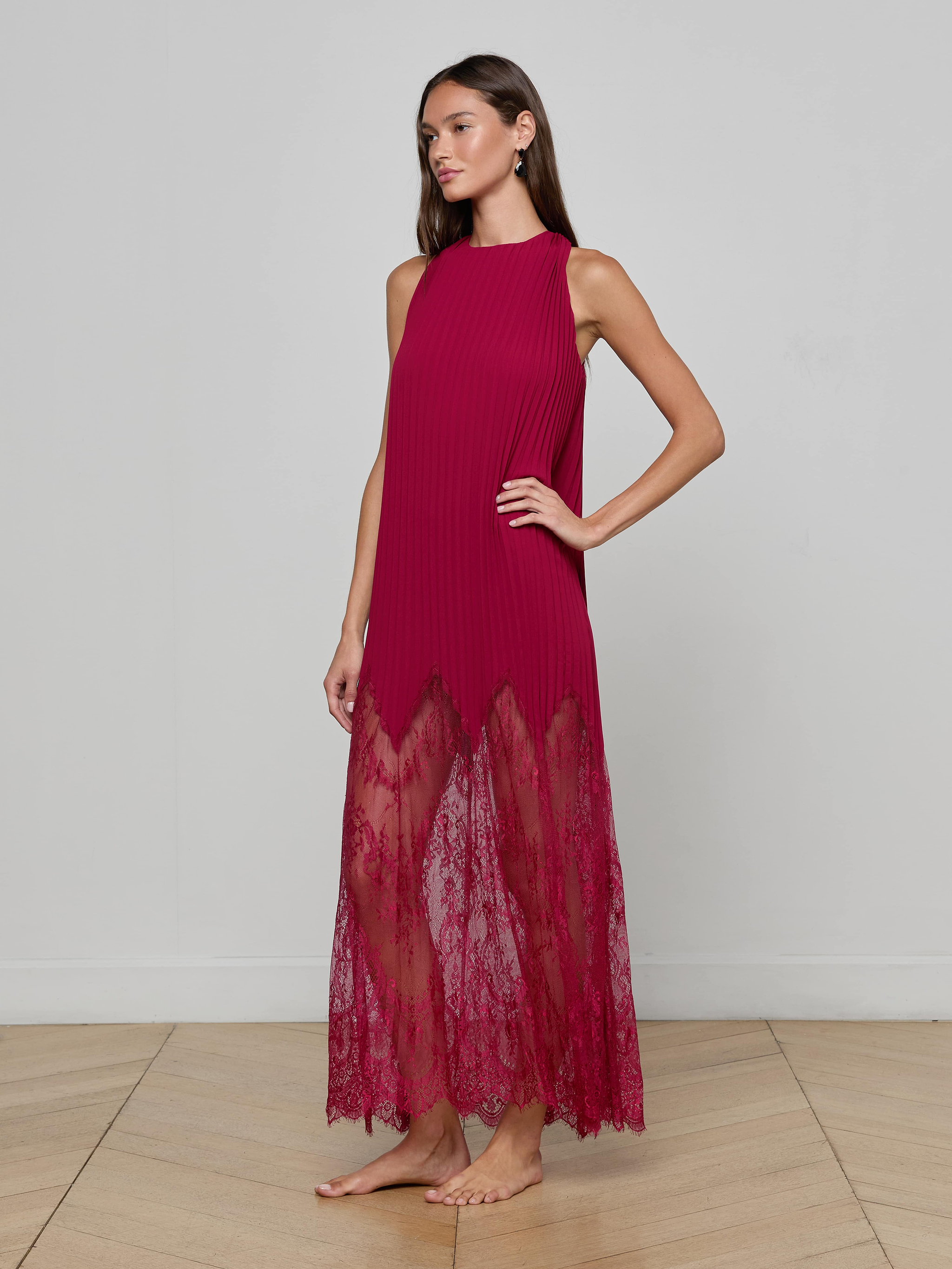 A woman stands barefoot wearing the Adalynn Cover-Up Dress, a sleeveless, floor-length red chiffon piece featuring a sheer lace hem. She poses with one hand on her hip against a plain white background.