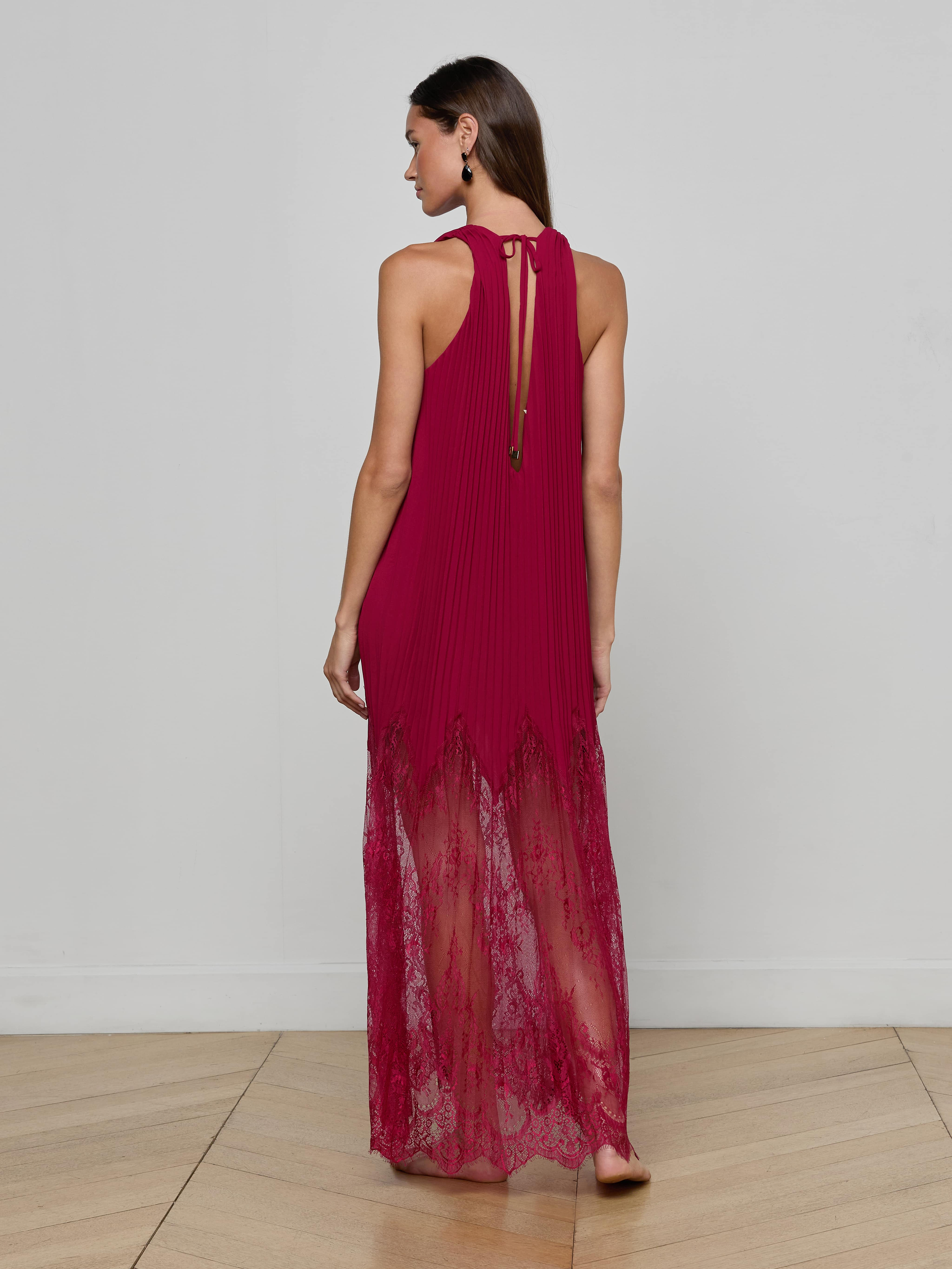 Barefoot and facing away, a woman models the Adalynn Cover-Up Dress—a sleeveless, floor-length red chiffon piece with delicate lace details—set against a plain white background; the perfect resort dress for your next getaway.