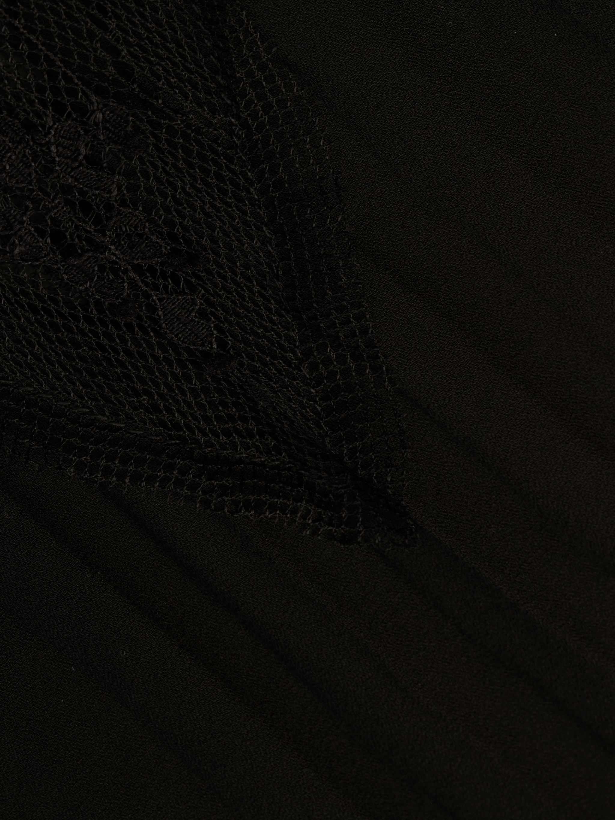 Close-up of the Sharon Cover-Up Pant in black, featuring a textured, triangular sheer lace overlay with intricate floral patterns on the left side, layered over smooth fabric.