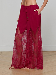 A person stands barefoot against a plain light background wearing the Sharon Cover-Up Pant, featuring sheer burgundy lace with a drawstring waist, pockets, and delicate sheer lace panels.